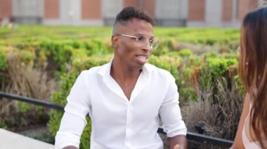 Afrikalı bir adam ve Latin bir kadın bir grup arkadaş arasında sokakta konuşuyorlar.