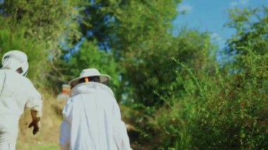 Arı kovanına doğru yürüyen iki koruma arıcısının arka görüntüsü