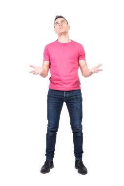 Pembe tişörtlü ve kotlu, üzgün bir erkek çaresiz bir şekilde yukarı bakıyor ve beyaz arka planda izole edilmiş zor bir durumda Tanrı 'dan yardım diliyor.