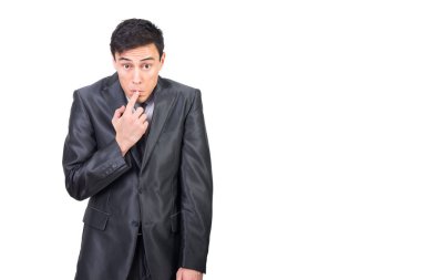 Resmi kıyafetli utangaç bir erkek omuzlarını silkerken dudaklarına dokunuyor ve beyaz arka planda durup kameraya bakarken suçluluk duyuyor.