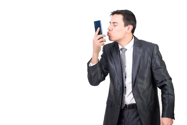 穿着正装 留着黑头发的男人一边吻着现代手机 一边站在白色背景下的中间镜头 — 图库照片
