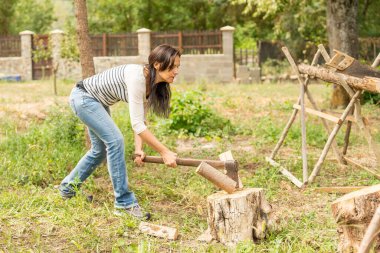 İnce ve zinde bir kadın bahçede odun kesiyor.