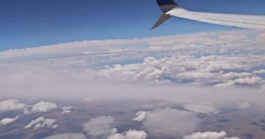 Mavi gökyüzünde, uçağın penceresinden uçan kanat manzarası.
