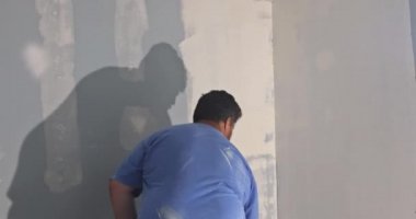 İç işleri için sıva uyguladıktan sonra duvarı tamir eden bir boya silindiri kullanan işçi.