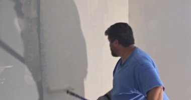 Ressamın arka görünüşü duvarı silindirle boyuyor.