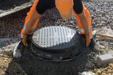 Yerdeki su kanalizasyonunun beton zeminine dökme demir kanalizasyon kapağı kuruluyor.