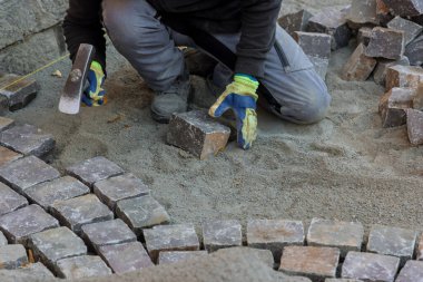 Yola taş döşeyen inşaat işçisi, yeniden inşa sürecinde kaldırımları indiriyor