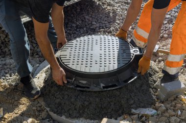 Bir işçi kanalizasyon inşaatı ile beton halkalardan yapılmış bir foseptik tankına kanalizasyon deliği kuruyor.