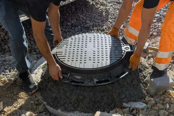 Bir işçi kanalizasyon inşaatı ile beton halkalardan yapılmış bir foseptik tankına kanalizasyon deliği kuruyor.