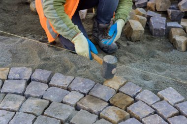 Kauçuk çekiç kullanan işçiler şehrin yakınındaki kaldırıma kaldırım taşları döşemek için taş kaldırımlar inşa ediyorlar.