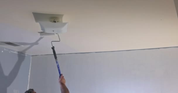 Vista trasera del pintor pinta el techo con un rodillo — Vídeos de Stock