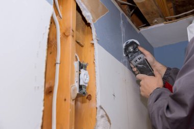 İnşaat elektrikli aletleriyle alçı tahtayı kesen işçinin hasar gören alçıpanı yerine ev yenileme servisi onarım çalışmaları