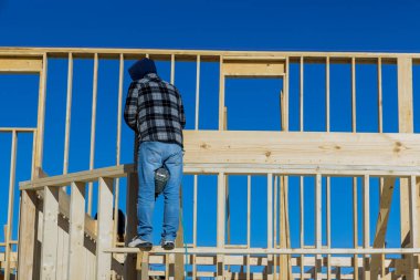 Beyaz koruyucu eldivenli işçiler, tahta tutuyorlar ve tahta kirişleri çivilemek için çekiç kullanıyorlar..