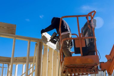 Beyaz koruyucu eldivenli işçiler, tahta tutuyorlar ve tahta kirişleri çivilemek için çekiç kullanıyorlar..