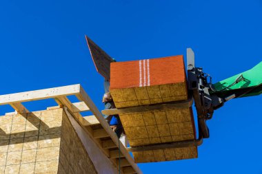 İnşaat işçisi altındaki ev çatıda hidrolik çekiç kullanarak ahşap çerçeveyi kontrplakla kaplıyor.