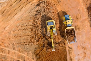 Kazıcıların hava görüntüsü inşaat alanında çalışıyor. Çöp kamyonlarına yüklemek için toprak dökülüyor.