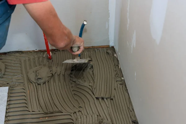 Aplicação de adesivo com espátula de pedreiro sobre piso para telha cerâmica — Fotografia de Stock