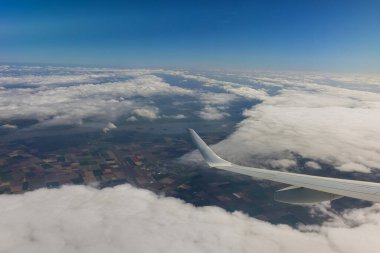Mavi gökyüzünde bulutlar, uçağın kanatlı penceresinden bir manzara.