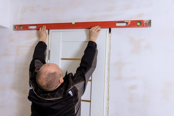 Carpenter at checks level correctness installation door — Stock Fotó