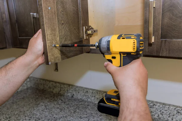 Worker hands fixing a hinge to a kitchen cabinet — стоковое фото