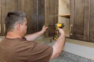 İşçi, dolapta tornavidayla yeni bir kabin yerleştirdi.