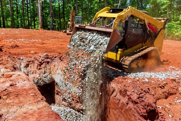 Patinaj direksiyon yükleyicisini kepçeyle kazıcı inşaat alanında çakıl boşaltıyor.
