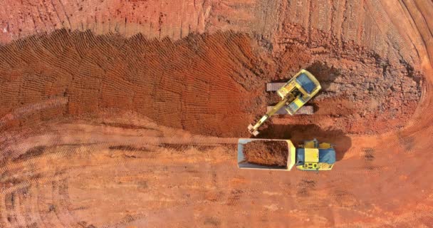 Vue aérienne du haut vers le bas d'une excavatrice chargeant de la terre dans un camion à benne basculante — Video