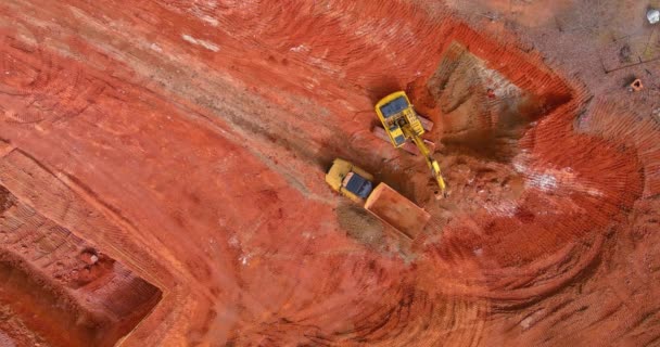 Una excavadora de orugas y un camión volquete de construcción de pie junto a ella mientras trabaja en la excavadora cava un hoyo y carga un camión volquete con tierra — Vídeo de stock