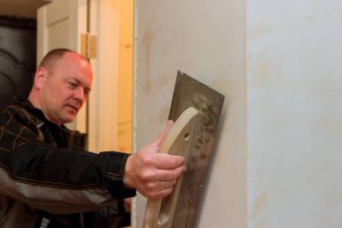 Alçıpan işçisi sıva, inşaat alanında kullanılan bir spatula ile duvarın seviyesini kontrol ediyor.