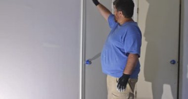 Müteahhit, yenilenme odası ve boya fırçası kullanarak ahşap bir kapıyı boyuyor.