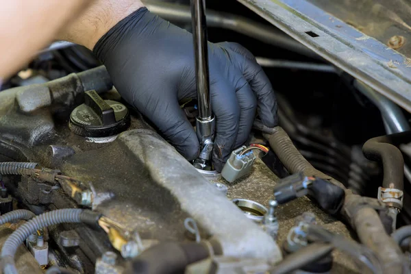 Auto mechanic makes repairs in garage service with unscrews old car candles are replaced for new spark plug