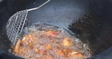 Şef ahşap bir kazanda tavuk kanadı kızartıyor. Yağ kaynayan aşçı tavuk kanatlarını ileri geri çırpıyor.