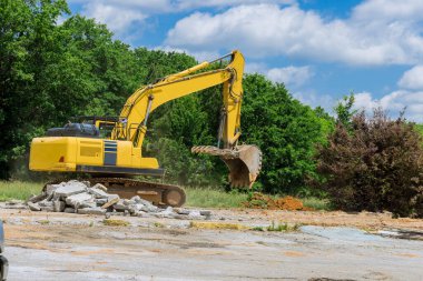 Bir kazıcı, inşaat alanındaki beton döşemeler için eski beton eziciyi parçalar ve parçalar.