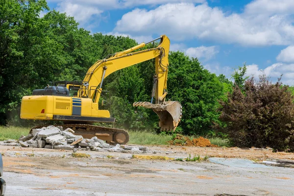 Bir kazıcı, inşaat alanındaki beton döşemeler için eski beton eziciyi parçalar ve parçalar.