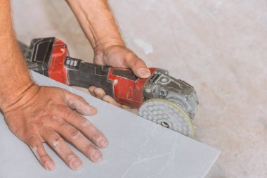 Bir işçi, banyo yenileme makinesinde elmas işlemeli bir diskle kesilmiş fayansların köşelerini parlatır.