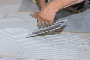 İşçi banyonun zeminine yapıştırıcı sürerken fayansları sürmeden önce ıslak havan topunu yayıyor.