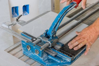 In construction worker cutting is using manual tools equipment to lay ceramic tiles on the floor during bathroom renovation