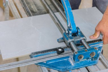 Seramik fayans zemininde, bir inşaat işçisi kiremitleri kesmek ve banyo tadilatı sırasında ekipmanların yardımıyla sermek için manüel bir alet kullanıyor.