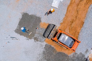 The bucket of an excavator being used for leveling gravel on the foundation of building at a construction site