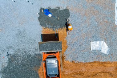 On construction site, a bucket from an excavator is leveling gravel at the foundation of a building