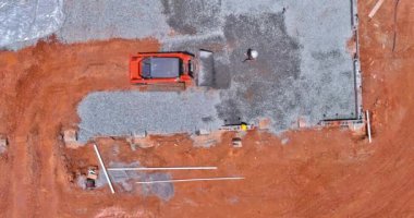 On construction site, a bucket from an excavator is leveling gravel at the foundation of a building
