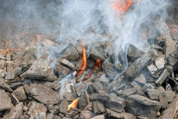 Using flaming hot charcoal to cook barbecue on a barbecue grill with burning bonfire outdoors