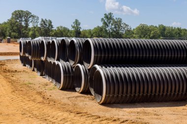 Yeni siyah plastik boru ve PVC kapağı kanalizasyon sistemi için inşaat sahasında sıralanmış.