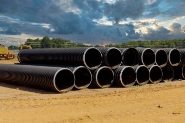 İnşaat alanındaki drenaj sistemleri için sıra sıra yığılmış siyah plastik PVC borular var..
