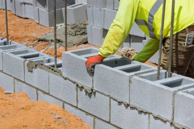 Bir duvar ustası inşaat alanındaki inşaat tekniklerini kullanarak havalanan beton bloklardan oluşan bir duvar inşa ediyor.
