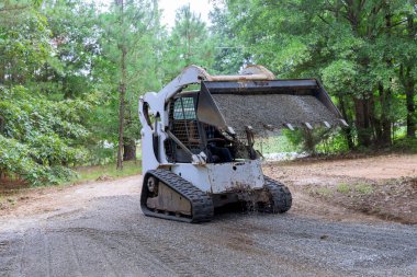 Eski bir yol yeniden inşa projesi, çakılları taşımak ve boşaltmak için vaşak traktörü kullanılmasını gerektirir
