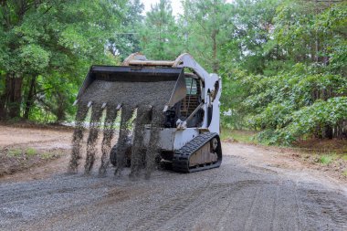 Mini yükleyici Bobcat traktörü eski yol yeniden inşa sahasında hareket ediyor ve çakılları boşaltıyor