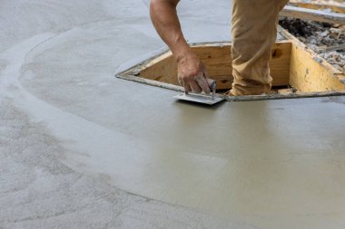 A construction worker using stainless steel edger on wet cement forming corner to new cement floor in construction site