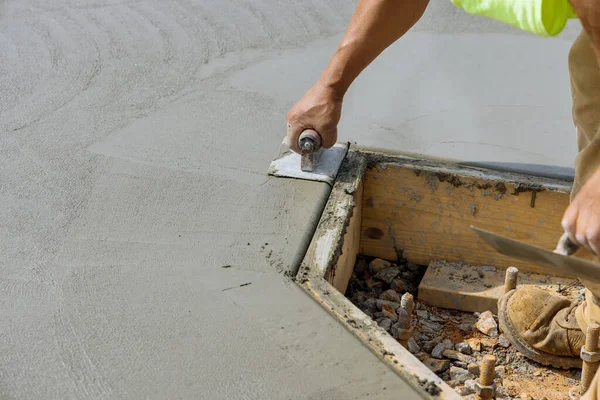 An employee of construction company uses a stainless steel edger to form corner in the new cement floor using wet cement