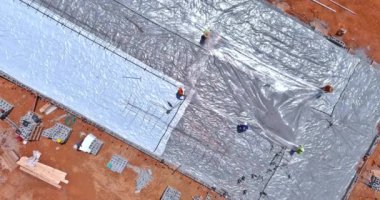 A barrier plastic will be installed before the concrete foundation of a building is poured, before the building can be completed